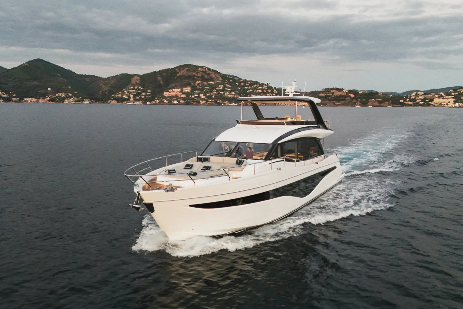 Le Princess Y72 au large devant une côte montagneuse, en fin de journée.