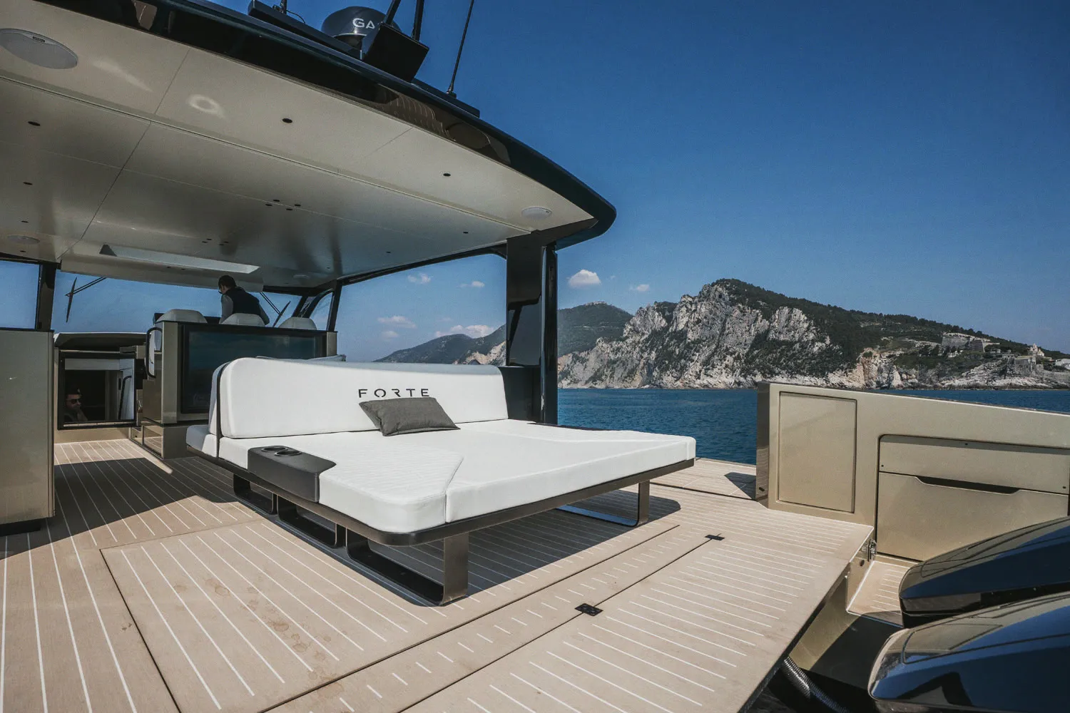 Le bain de soleil avant sous le hardtop, pont en teck et côte à l'horizon.