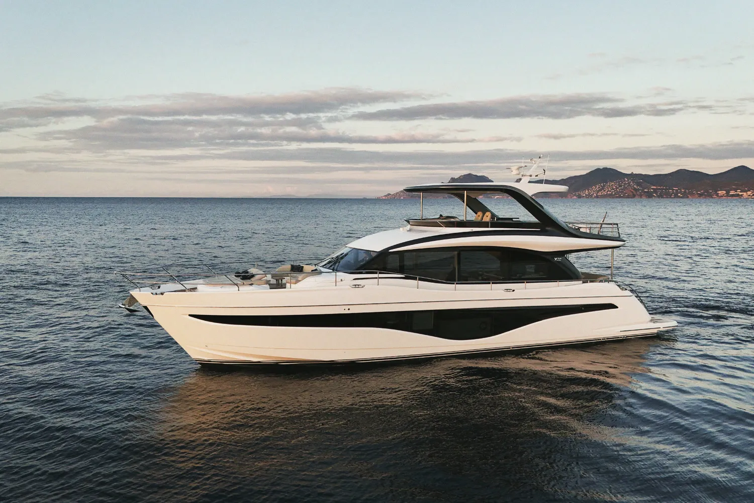 Le Princess Y72 immobile sur une mer d'huile, reflets et côte à l'horizon.