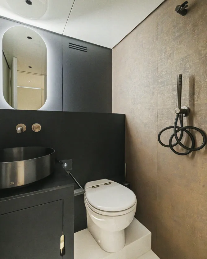 Une salle d'eau : vasque ronde, miroir et rangements sombres.