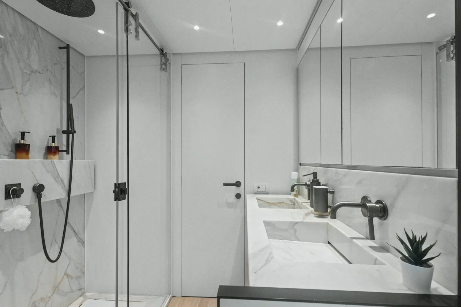 Une salle d'eau : marbre clair, douche à l'italienne et double vasque.