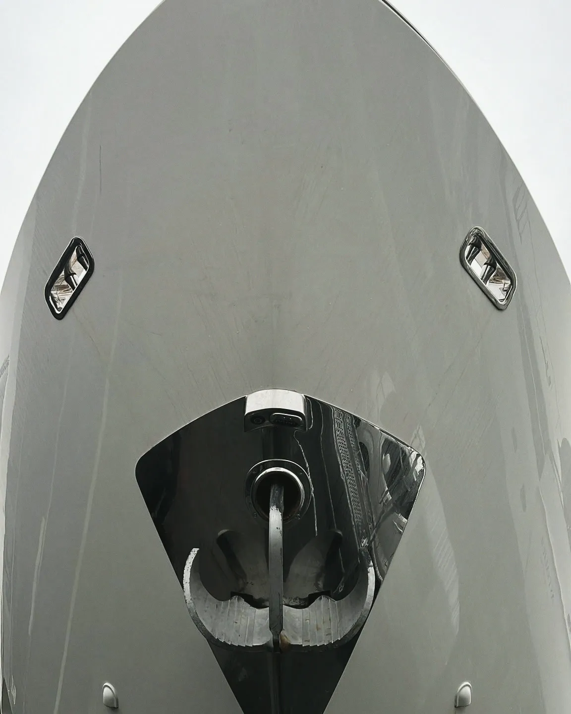 Étrave d'un yacht vue de face : l'ancre logée dans son puits d'inox à l'avant de la coque, deux ouvertures chromées de part et d'autre.