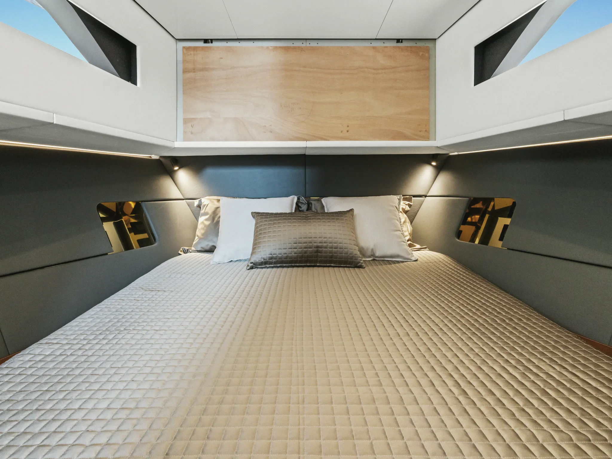 Une cabine : couchage double, tête de lit en bois clair et custodes de coque.