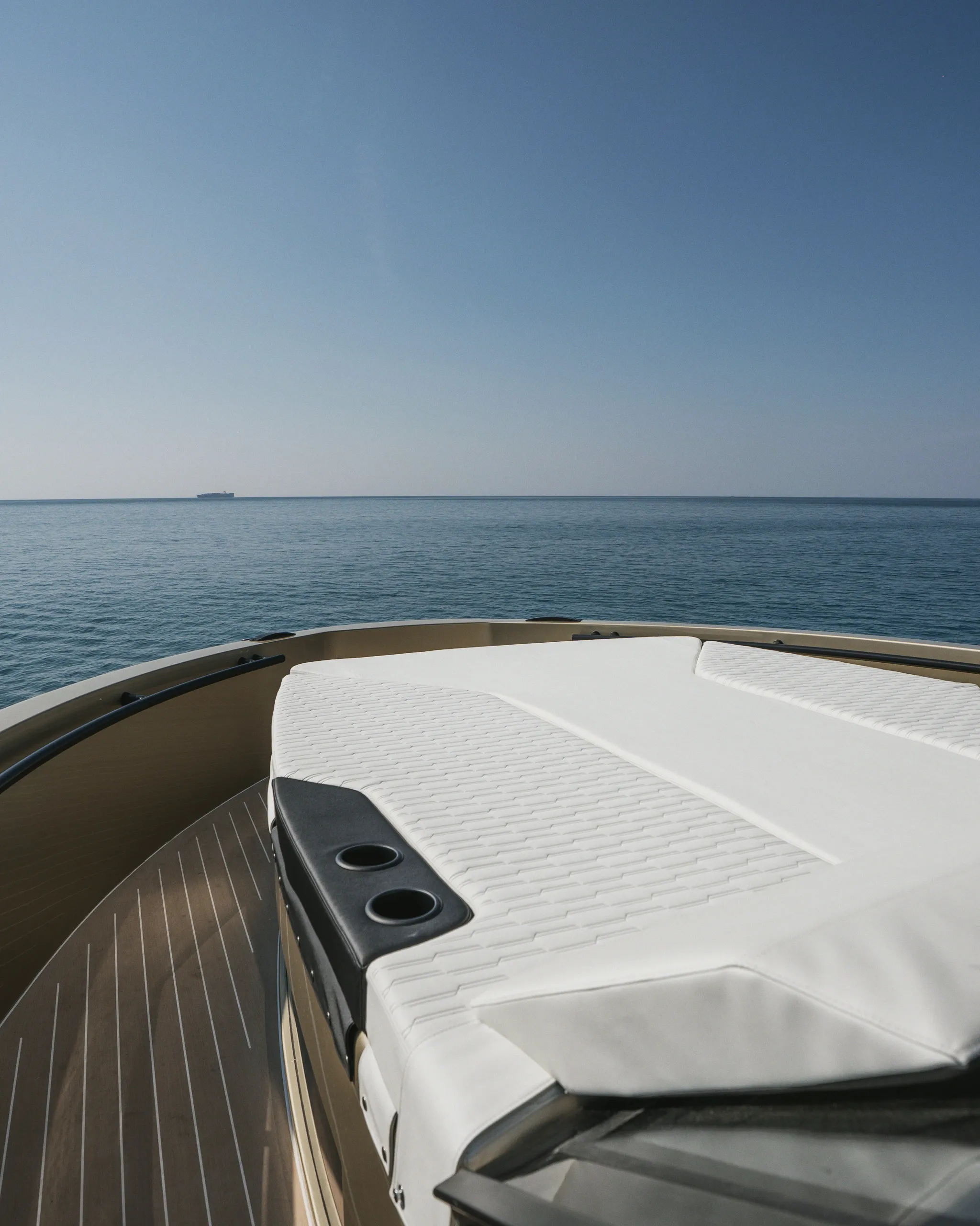 Plage avant d'un yacht : bain de soleil blanc, pont en teck, mer ouverte et ciel dégagé jusqu'à l'horizon.