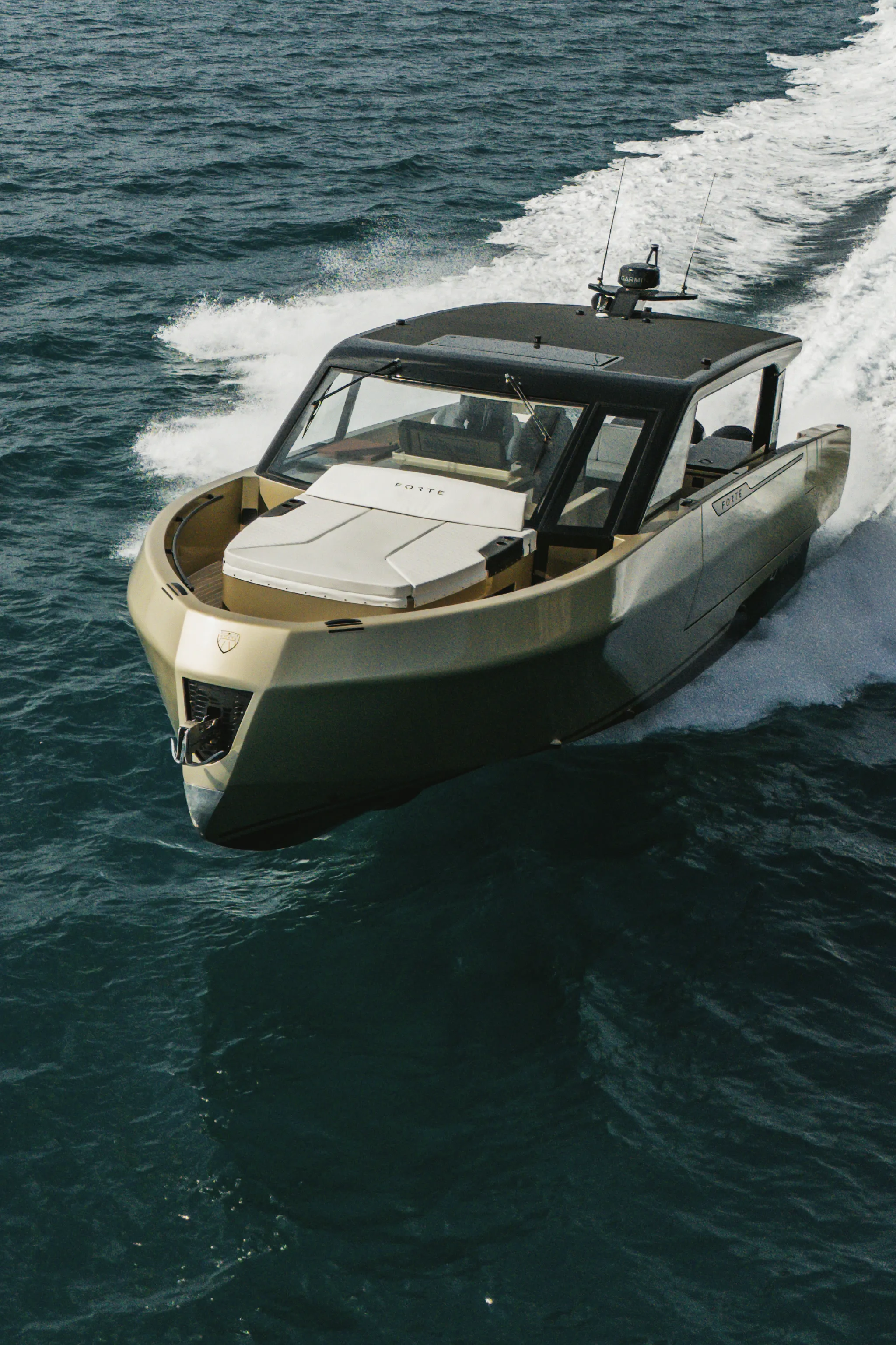 Yacht à moteur vu du ciel, en marche sur une mer ouverte : hard-top sombre, bain de soleil clair sur la plage avant, sillage d'écume derrière la poupe.
