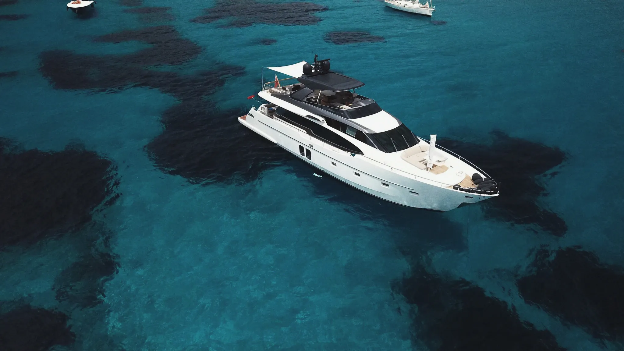 Vue aérienne d'un yacht au mouillage sur une eau turquoise, un voile d'ombrage tendu au-dessus du pont arrière.